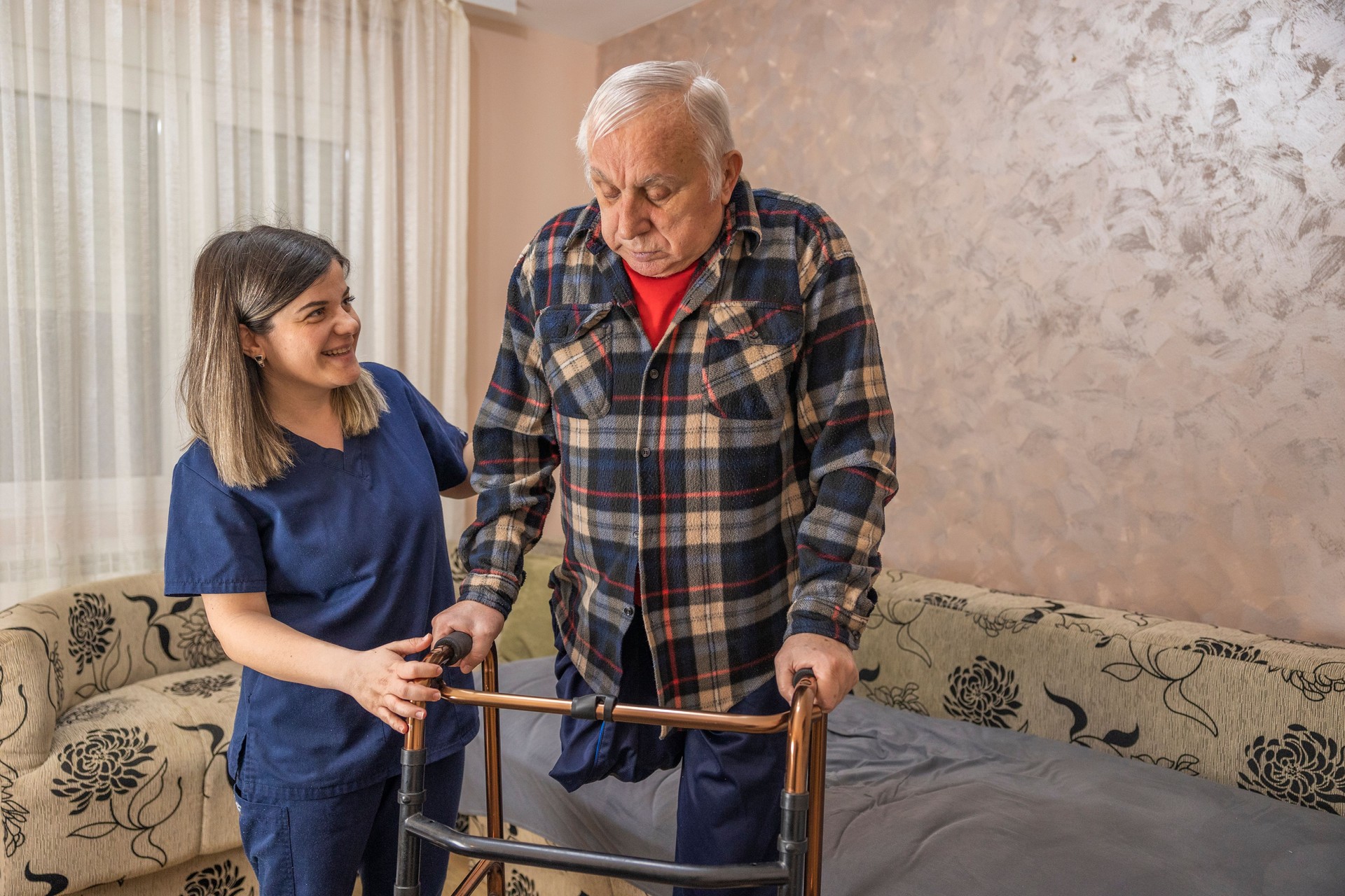 Assistant helping senior man walking with mobility walker at home